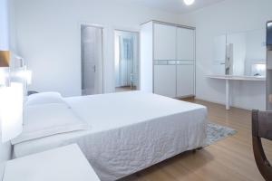 a white bedroom with a large bed and a kitchen at Hotel Gracher Brusque in Brusque