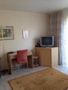 ein Wohnzimmer mit einem TV und einem Schreibtisch mit einem roten Stuhl in der Unterkunft Guesthouse AirMinis in Düsseldorf