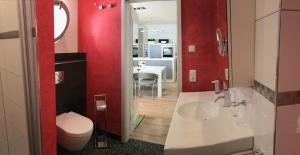 ein Bad mit einem Waschbecken, einem WC und roten Wänden in der Unterkunft Exclusive FEWO in Warnemünde, 150m to the beach, 2 bathrooms, 2 bedrooms, sauna, WiFi and much more. in Rostock