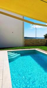 a swimming pool with blue water and a yellow umbrella at Holiday house NiRi with a heated outdoor pool /BBQ in Kaštela