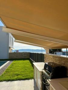 eine Terrasse mit einem Dach mit Grill und Gras in der Unterkunft Holiday house NiRi with a heated outdoor pool /BBQ in Kaštela