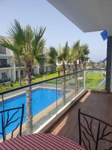 uma varanda com vista para uma piscina e palmeiras em Great appartement vue sur mer et piscine em Dar Bouazza