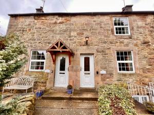 a stone house with a white door and two chairs at Jewel Cottage in Matlock