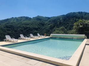 a swimming pool with chairs and mountains in the background at Gîte Olivier in Vals-les-Bains