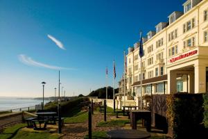 a hotel with tables and benches next to the ocean at Bournemouth Highcliff Marriott Hotel in Bournemouth
