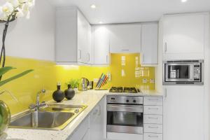 cocina con armarios blancos y fregadero de acero inoxidable en Chelsea - Draycott Place by Viridian Apartments, en Londres