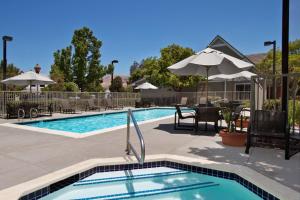 una piscina con mesas, sillas y una sombrilla en Residence Inn Milpitas Silicon Valley, en Milpitas