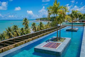a swimming pool with palm trees and the ocean at Unity Suites Beira Mar in João Pessoa