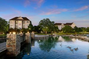 a group of ducks swimming in a river in front of buildings at Residence Inn Des Moines West at Jordan Creek Town Center in West Des Moines