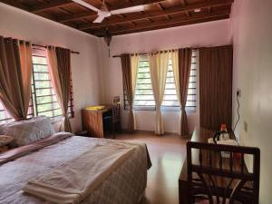 een slaapkamer met een bed, een bureau en ramen bij VanaJyotsna Forest Home in Maraiyūr