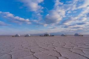 a cracked desert field with domes in the background at Salinas Grandes Jujuy - Pristine Luxury Camp in Salinas Grandes
