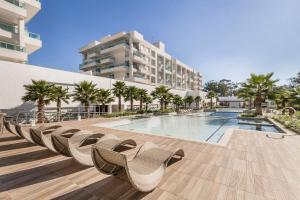a swimming pool with chairs and a building at Atlântida Green Square - 601B in Capão da Canoa