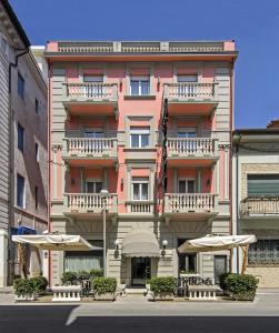 un bâtiment rose avec des tables et des parasols devant lui dans l'établissement Hotel Katy, à Viareggio