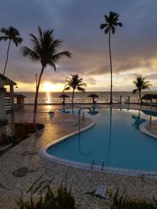 una piscina con palmeras y el océano al atardecer en Chale 48 Maragogi Village Gales en Maragogi