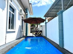 a swimming pool with an umbrella next to a house at Bandar Melaka Family Bungalow Private Pool BBQ WiFi Netflix in Melaka