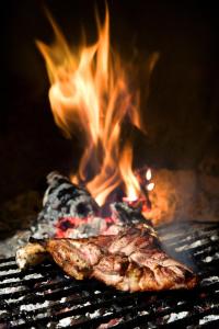 un trozo de carne cocinándose en una parrilla con llamas en Hostal Las Rumbas, en Nuévalos