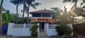 a small house with a white fence and palm trees at Happy Seas Beach Villa in Alleppey