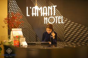 L'amant de Hanoi Hotel - khách sạn Lamant de Hà Nội في هانوي: امرأة تتحدث على الهاتف على طاولة مع الكمبيوتر المحمول