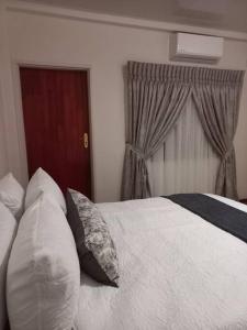 a bedroom with a white bed with pillows and a window at Ribbon 210's Two bedroom apartment in Gaborone