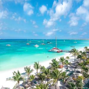 a beach with palm trees and boats in the water at Aruba Family Oasis 2BR Pool 3min Walk to Eagle Beach in Palm-Eagle Beach