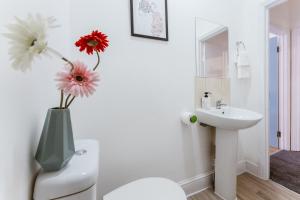 une salle de bains blanche avec un vase et des fleurs. dans l'établissement Mile end Double rooms 86a, à Londres