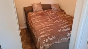 a bed with a brown comforter with writing on it at PEMATRA Ferienwohnung Strandmuschel in Travemünde