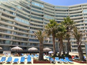 uma praia com cadeiras e palmeiras e um grande edifício em San alfonso timonel em Algarrobo