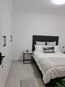 a white bedroom with a large bed and a table at Cozy 2 bedroom APT - Near Kenilworth Racecourse in Cape Town