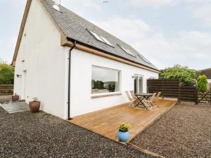 a white cottage with a wooden deck in front of it at Lurach House in Port Appin