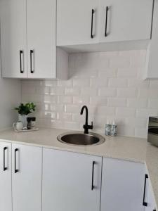 una cucina bianca con lavandino e armadietti bianchi di Cozy 2 bedroom APT - Near Kenilworth Racecourse a Città del Capo