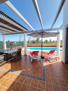 patio z parasolem i krzesłami oraz basenem w obiekcie Villa Eva - New to the market, fully refurbished licensed villa - private pool w mieście Caleta De Fuste