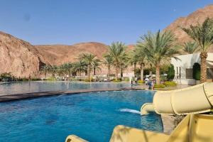una piscina con palmeras y montañas en Norjan Condo Apartment, en Áqaba