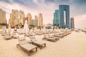 einen Strand mit Liegestühlen, Sonnenschirmen und Gebäuden in der Unterkunft Super Elegant studio apartment-Sparkle tower By SWEET HOMES in Dubai
