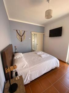 a bedroom with a white bed and a television at Apartamento Vicentino in Vila Nova de Milfontes