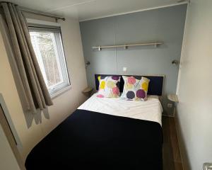 um pequeno quarto com uma cama com almofadas e uma janela em Mobil homme proche de la mer em Le Grau-du-Roi
