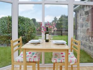 a wooden table with two chairs in front of a window at Dairy Cottage - Beaufort Estate in Belladrum