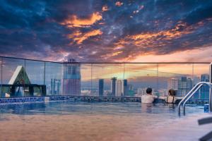 a man and woman in a infinity pool with a city skyline at Luxcity Hotel & Apartment in Phnom Penh