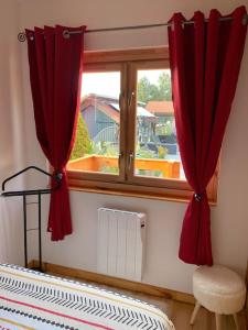 una ventana con cortinas rojas y una silla en una habitación en Chalet 2 personnes avec jacuzzi et piscine saisonnière en Corcieux