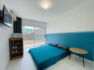 ein Schlafzimmer mit einem blauen Bett, einem Tisch und einem Fenster in der Unterkunft REA Lodge in Punaauia