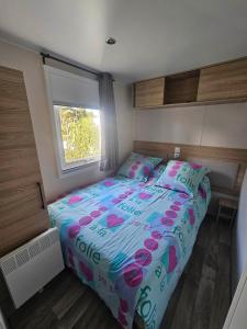 a bedroom with a bed with pink and blue sheets and a window at Mobil home Sylvie et Alain in Canet-en-Roussillon