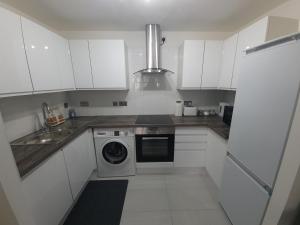 2 bedroom light, spacious aptmnt nr Heathrow في Cranford: مطبخ بدولاب بيضاء وغسالة ملابس