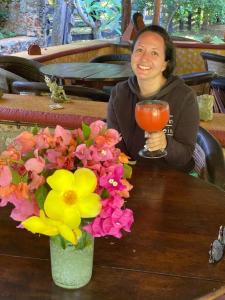 een vrouw aan een tafel met een drankje en bloemen bij Cabañas Maya Aire 