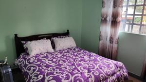 uma cama roxa com almofadas brancas e uma janela em Camp-Flo 3br Guest House-Eldoret em Eldoret