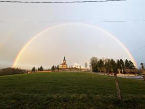 un arco iris sobre un campo con una iglesia en el fondo en LE CEDRE BLEU, en Saint-Michel-sur-Meurthe
