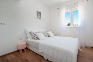 a white bedroom with a white bed and a window at Apartman Kiara in Rogoznica