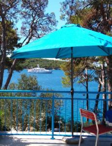 a blue umbrella and a chair with a boat in the water at Casa Liliana By the Sea in Mali Lošinj