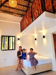 a woman and two children sitting on a bed at Cozy Cabin Casita Anahaw in Indang