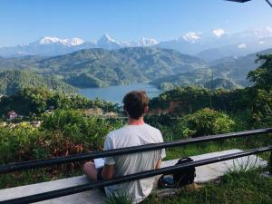a man sitting on a bench looking at a mountain view at Mountain View Eco Farm in Rānīpauwa