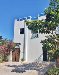 ein weißes Haus mit einer Tür und einem Baum in der Unterkunft Hostel Humanity in Puerto Morelos