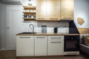 La cuisine est équipée de placards blancs, d'un évier et d'une cuisinière. dans l'établissement WiguryTower Apartaments 66', à Łódź